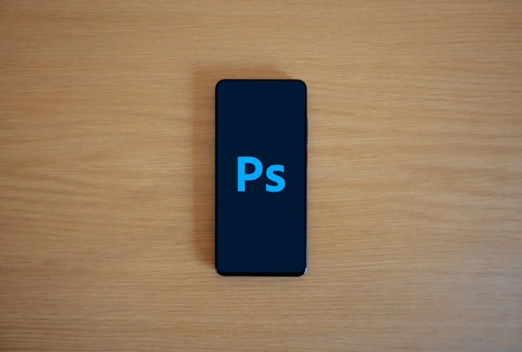 Modern smartphone on a white desk displaying a photo editing app with background removal feature, surrounded by coffee cup and notebook, bright office lighting from above, overhead flat-lay view, product photography, crisp and clean aesthetic