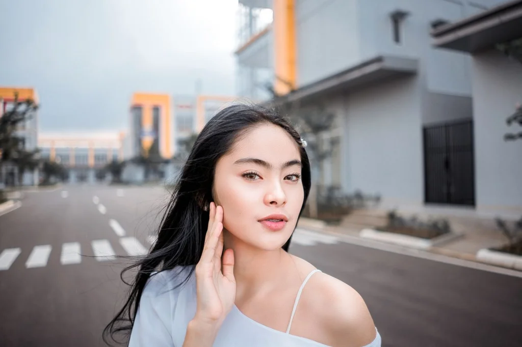 Woman in her late 20s with long black hair examining a blurry photo on her laptop screen, frustrated expression, sitting at a white desk in a bright home office, soft window light from the right, close-up over-shoulder shot, lifestyle photography, shallow depth of field