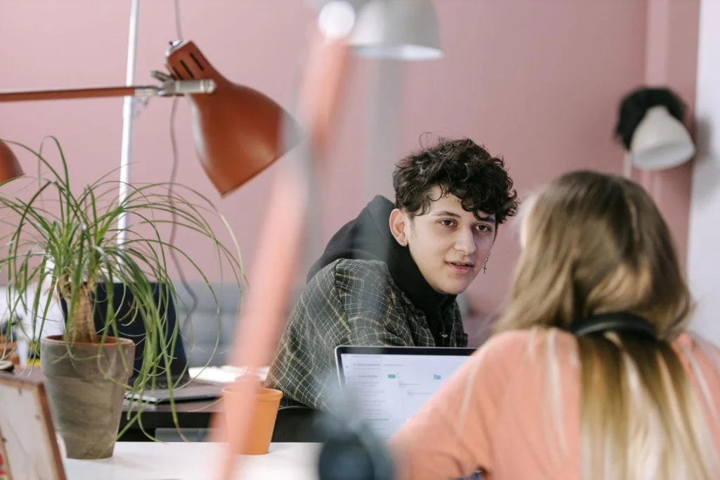 Creative workspace showing laptop with face swap software interface, digital tablet, and multiple printed photos scattered on desk, overhead flat lay view, bright daylight, editorial product photography