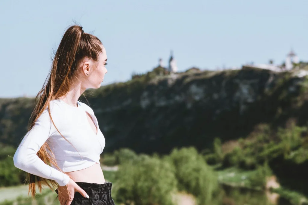 Woman in her late 20s with medium brown hair in a ponytail, holding smartphone at arm