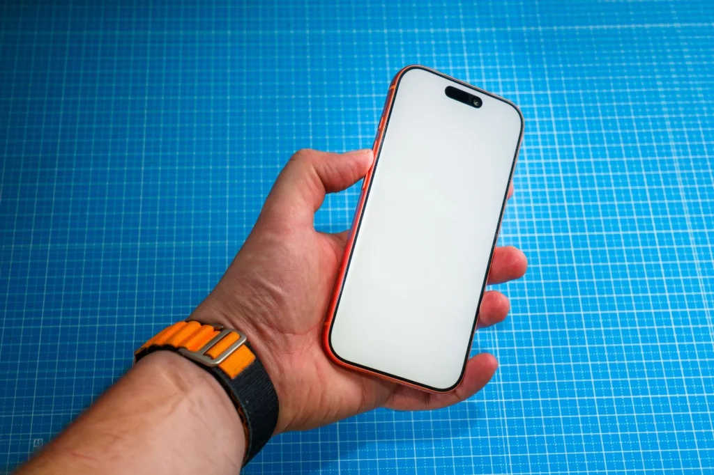 Close-up hands holding smartphone with camera grid lines visible on screen, showing rule of thirds composition with landscape in background, golden hour lighting, shallow depth of field, overhead angle at f/2.8, editorial photography style