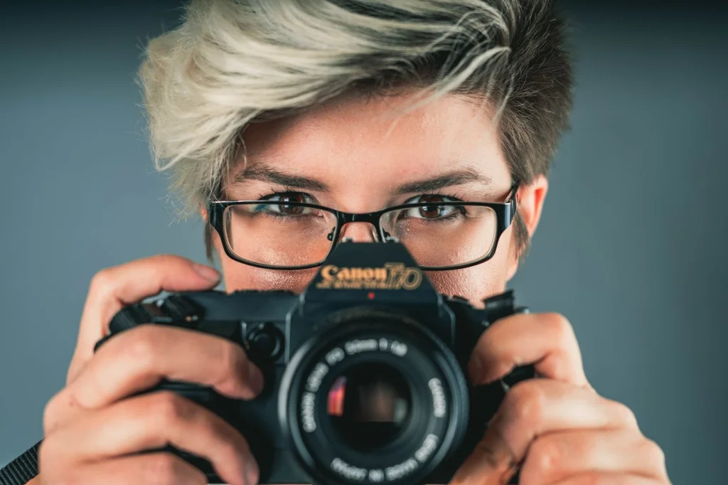 Photographer in her 40s with short blonde hair examining before-and-after photos on a large monitor, split screen showing low-res and enhanced versions, modern office with camera equipment, bright LED lighting, close-up shot, professional photography