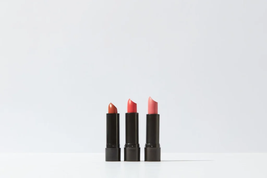 Makeup products floating with clean white background, red lipstick, gold eyeshadow palette, black mascara, soft studio lighting from above, overhead product shot, commercial photography, f/8 crisp focus