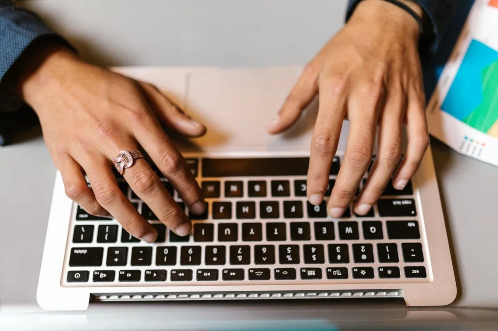 Close-up of hands typing on keyboard with multiple browser tabs open showing different background removal tools, smartphone nearby displaying photo editing app, warm desk lamp lighting, macro shot at f/4, lifestyle photography, modern workspace