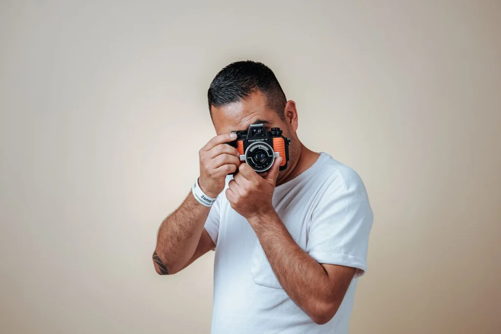 Professional photographer in his 30s with short brown hair wearing a grey t-shirt, removing background from product photos on a MacBook Pro at a clean white desk with coffee mug, soft window light from the right, eye-level medium shot, lifestyle photography, shallow depth of field