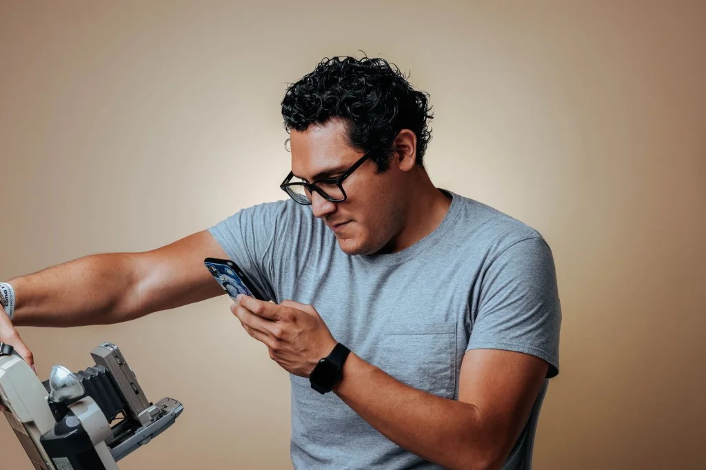 Professional photographer in his 40s with glasses, black shirt, focused expression, using tablet at a modern studio with softbox lighting equipment, warm tungsten light from the right, medium shot at f/1.8, commercial portrait, bokeh background