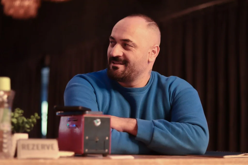 Happy entrepreneur in his 30s with beard, navy blue shirt, proud smile, standing next to a large monitor displaying before/after comparison of product photos with transparent backgrounds, modern office with glass walls, soft LED lighting, three-quarter view, business portrait style, professional depth of field
