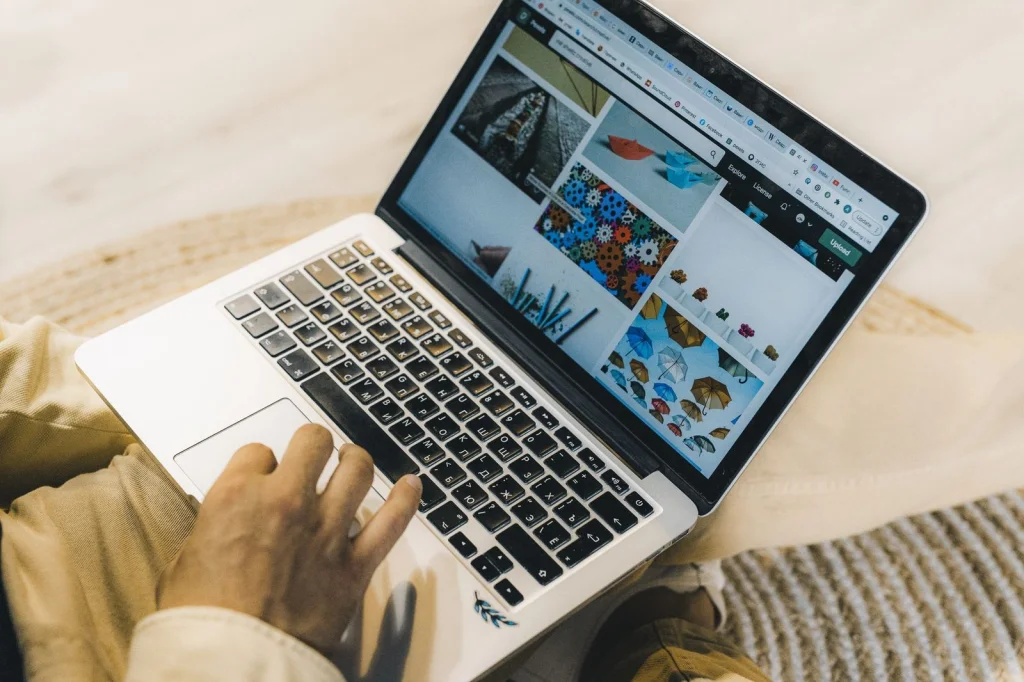 Hands of a graphic designer working on a laptop, screen showing photo editing interface with background removal tool, clean white desk setup with coffee cup, warm desk lamp lighting, overhead angle, workspace photography, shallow depth of field