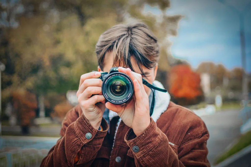 Professional photographer in his 30s with dark hair using Adobe Photoshop on a 27-inch monitor, pointing at background removal tools panel, modern office setting with plants, soft LED panel lighting, over-shoulder shot showing screen, editorial portrait, shallow depth of field