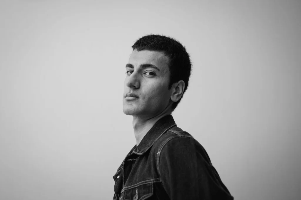 Man in his 30s with short dark hair, white collared shirt, neutral expression, standing against white background, even studio lighting, eye-level headshot, passport photo style, sharp focus