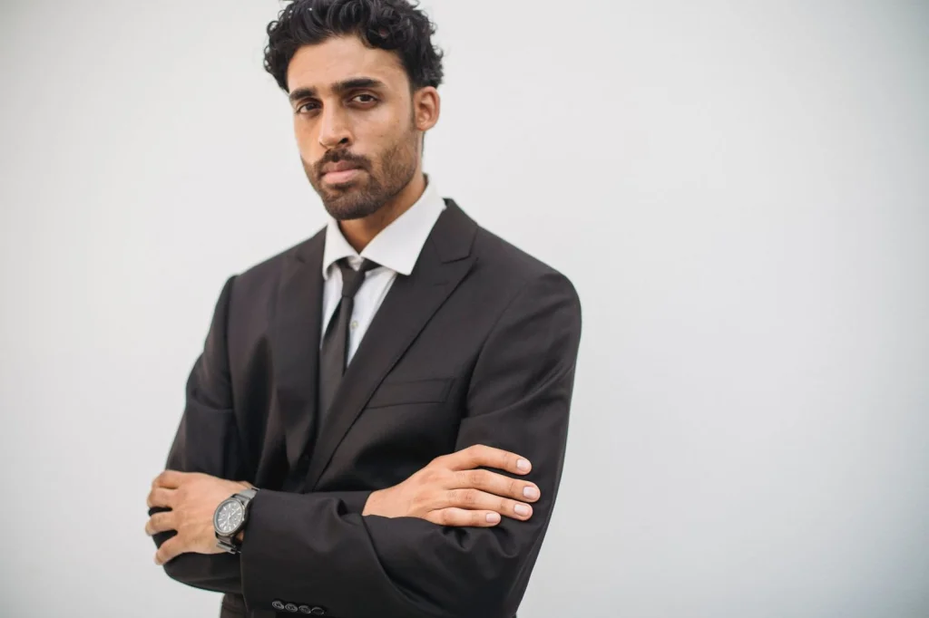 Young professional man in dark suit and tie, clean-shaven with short black hair, serious expression facing camera, plain white studio background, professional portrait lighting from front and sides, medium shot headshot, corporate headshot style, crisp focus