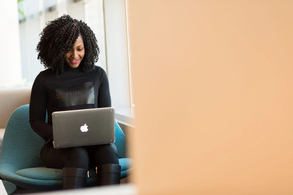 Female social media manager in her late 20s with curly hair, colorful blazer, concentrated expression, working on Instagram posts with transparent background images on a large monitor, bright coworking space with plants, natural daylight from large windows, medium shot from side angle, modern workspace photography