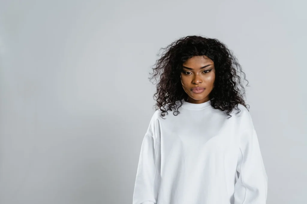 Woman in her 20s with curly black hair, white t-shirt, holding a smartphone, sitting at a modern cafe with exposed brick walls, natural window light from the right, medium shot at eye level, lifestyle photography, shallow depth of field