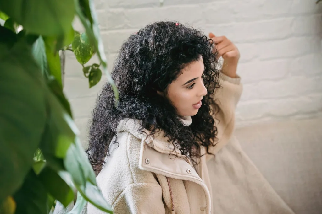 Young woman in her 20s with curly black hair, wearing a bright yellow sweater, standing against a colorful graffiti wall, soft overcast lighting, medium shot from waist up, lifestyle portrait with shallow depth of field