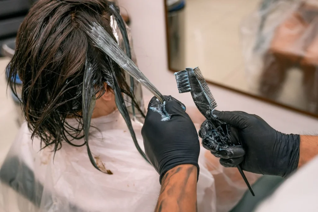 Professional hairstylist in her 40s with black hair in a sleek bob, examining a tablet showing AI hairstyle results, modern salon with mirror backdrop, warm overhead lighting, medium shot from the side, commercial photography, shallow depth of field
