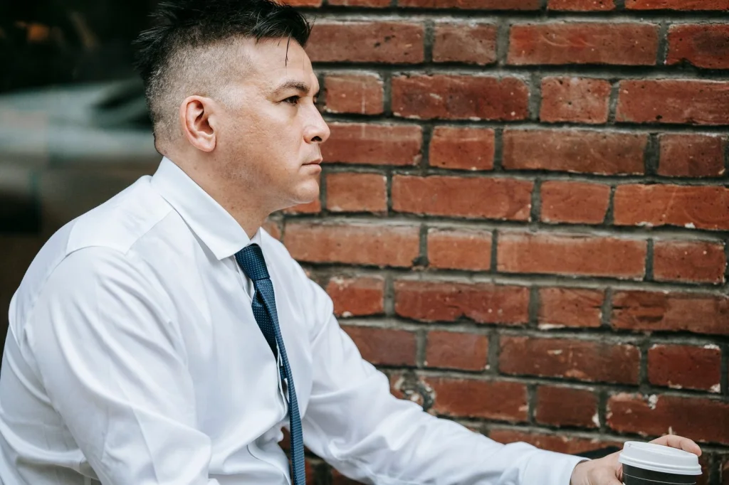 Business professional in his late 20s with modern haircut, wearing navy blue blazer over light blue dress shirt, confident smile looking directly at camera, contemporary glass office building interior with soft natural lighting, chest-up portrait at eye level, editorial business photography, shallow depth of field