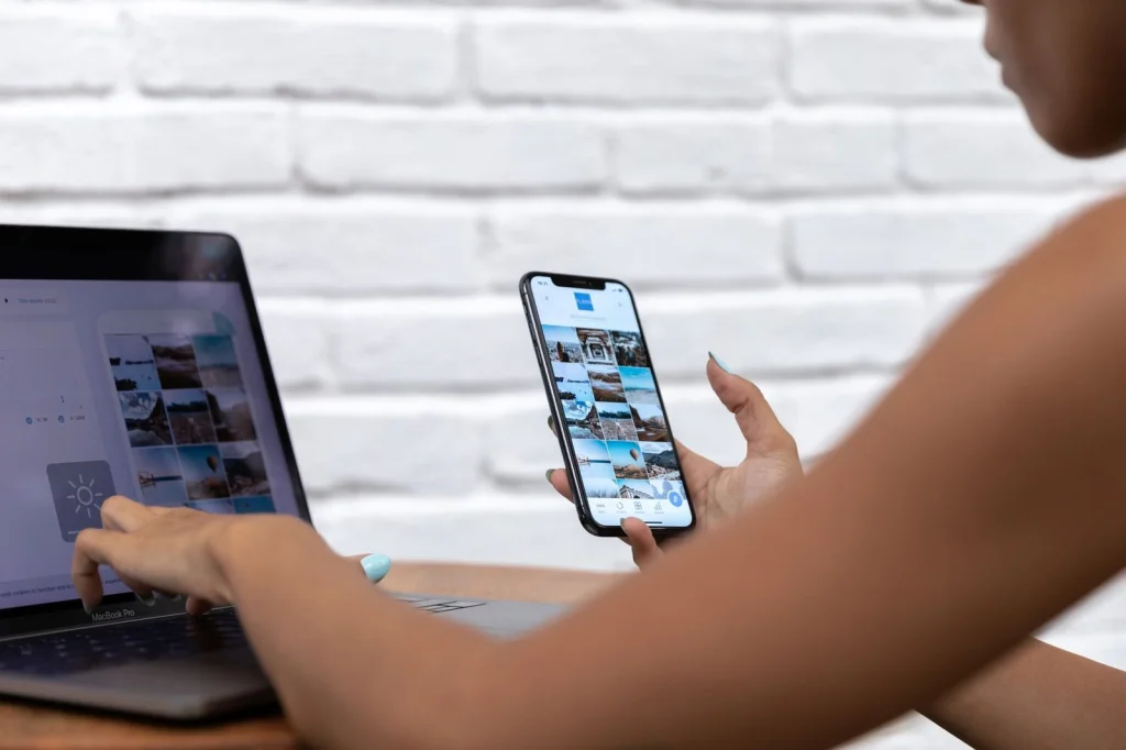 Freelance content creator in her 20s with laptop and smartphone, surrounded by printed AI-generated images spread on a wooden desk, warm natural lighting, overhead flat lay angle, lifestyle workspace photography