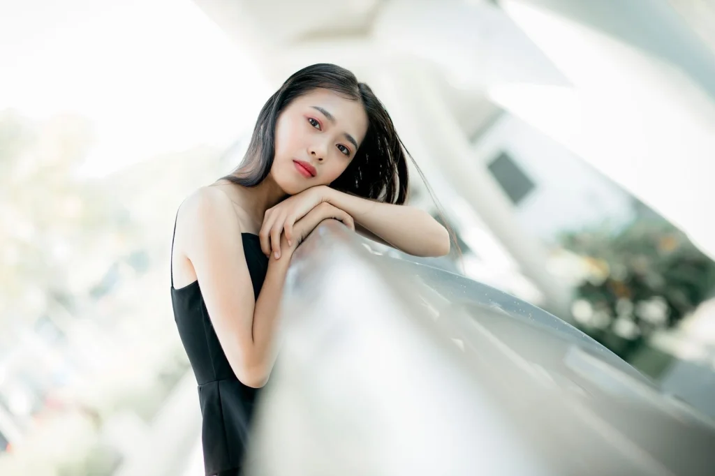 Professional headshot of Asian woman in her 30s with sleek black hair in a long bob, subtle smile, sitting in modern office with city view, soft natural lighting from large windows, three-quarter view medium shot, corporate portrait, crisp focus