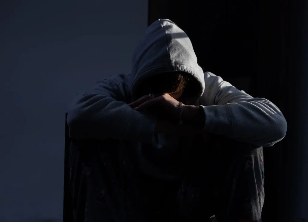 Person in their 30s wearing a gray hoodie, sitting on a modern couch with phone in hand, concentrated expression while editing a photo on Adobe Express mobile app, warm living room lighting with a floor lamp in the background, medium shot at f/2.8, candid lifestyle photography