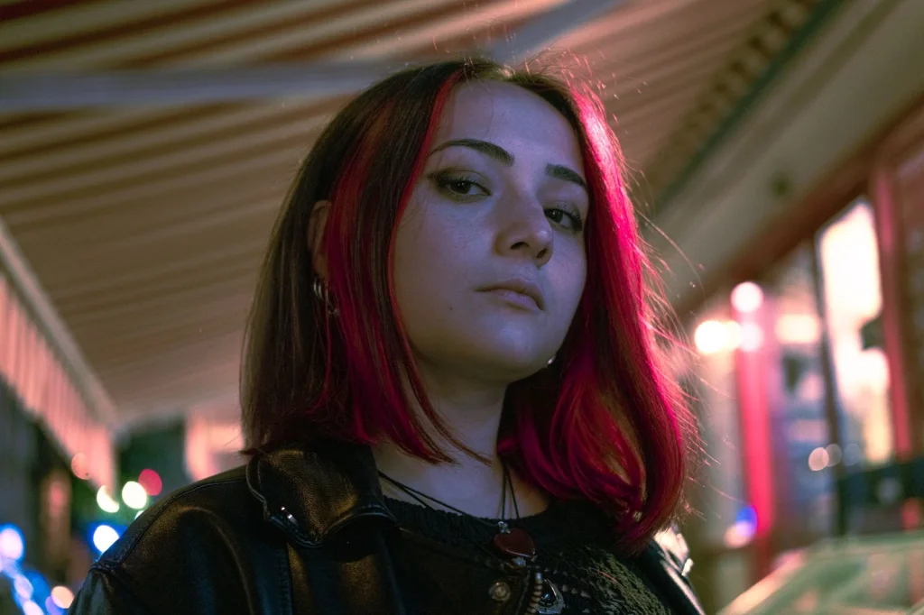 Digital artist in her late 20s with colorful hair, working on a tablet with stylus, surrounded by AI-generated artwork prints on the walls, warm LED lighting, overhead angle showing workspace, creative studio photography