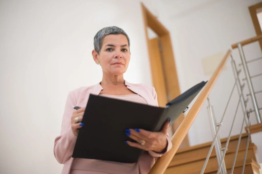Businesswoman in her 40s with short black hair, wearing a navy blue blazer, confident smile, sitting at a modern office desk with city skyline in background, soft professional lighting from the right, three-quarter angle medium shot, corporate headshot style