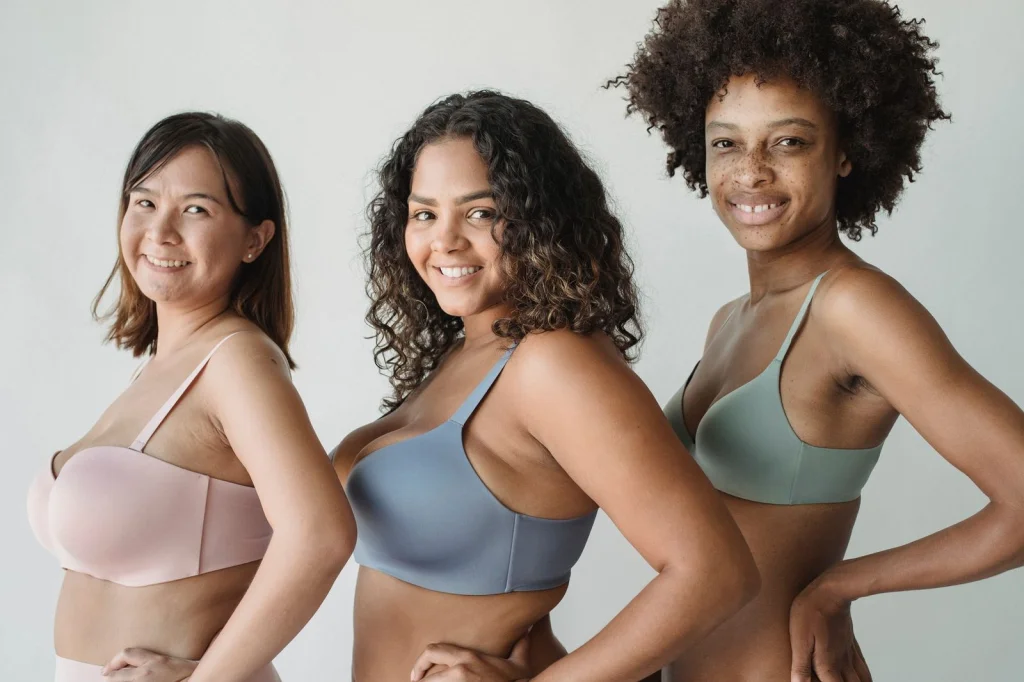 Diverse group of three women with different curl patterns 2C, 3B, and 4A hair, standing together against white studio backdrop, each holding phones showing hair app results, bright studio lighting, wide shot at chest level, commercial photography, clean modern aesthetic