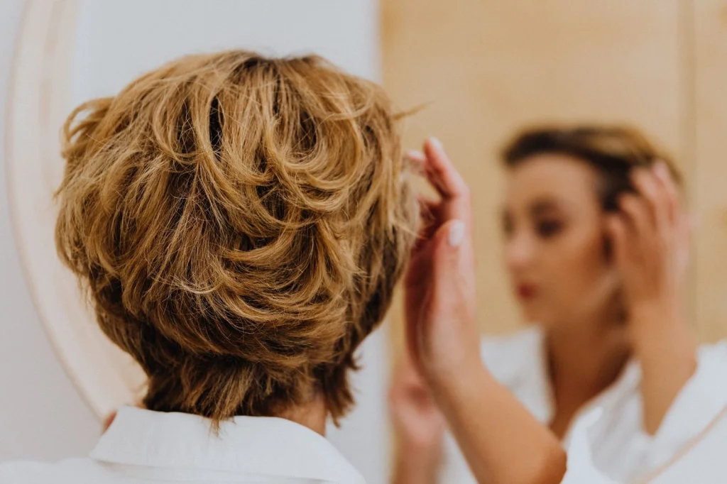 Professional woman in her 40s with short blonde bob haircut, neutral expression, wearing white button-up shirt, standing against plain white studio background, soft even studio lighting from front, eye-level headshot, editorial portrait, crisp focus