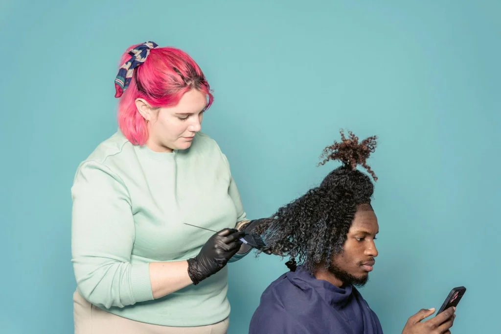 Professional hairstylist in modern salon showing smartphone with virtual hairstyle to female client, both looking at screen and discussing, salon chair and mirrors in background, soft salon lighting, medium shot at f/2.8, editorial photography style