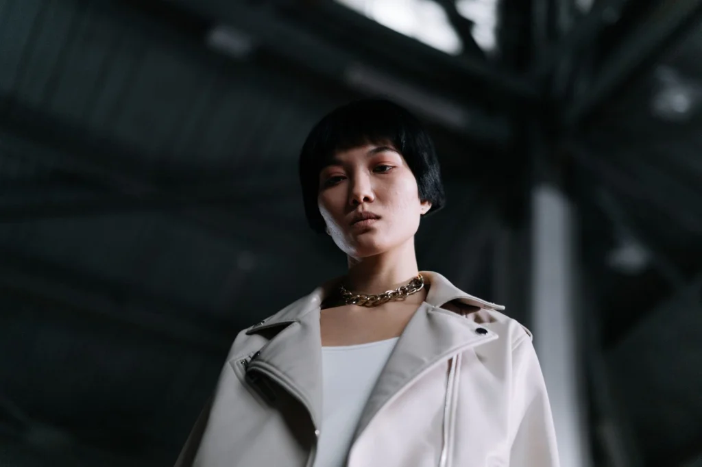 Woman in her 20s with short black hair looking frustrated at a pixelated photo on her laptop screen, sitting at a white desk with morning sunlight streaming through window, medium shot from slight angle, editorial portrait, shallow depth of field