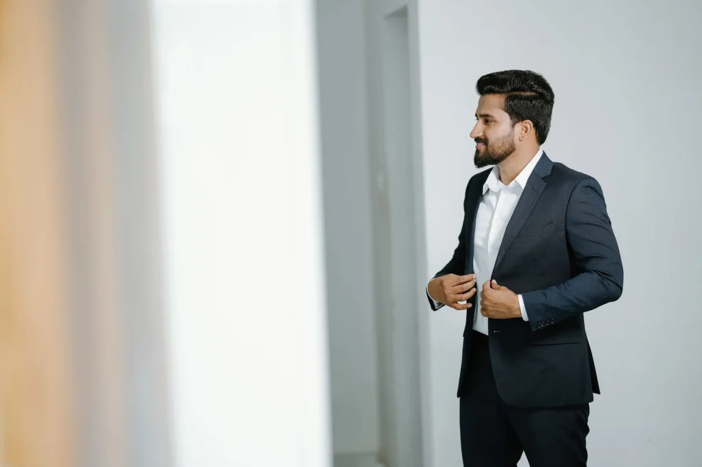 Male professional in dark charcoal suit with white dress shirt and blue tie, serious expression, standing against crisp white studio background, even soft lighting from multiple angles, eye-level portrait, corporate photography style