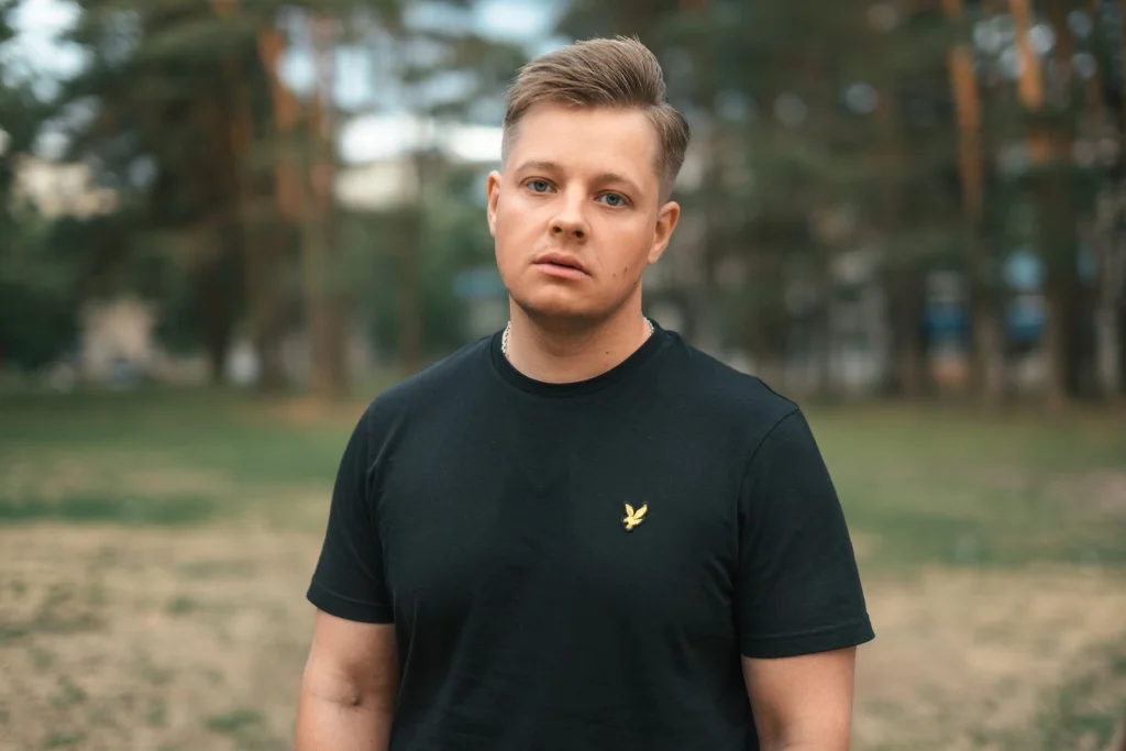 Young man with short blonde hair looking at mirror reflection showing different hairstyle, modern barbershop with brick walls, warm overhead lighting, side profile medium shot, cinematic depth of field