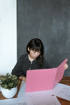 Awomaninablackandwhiteshirtislookingatapinkbook.